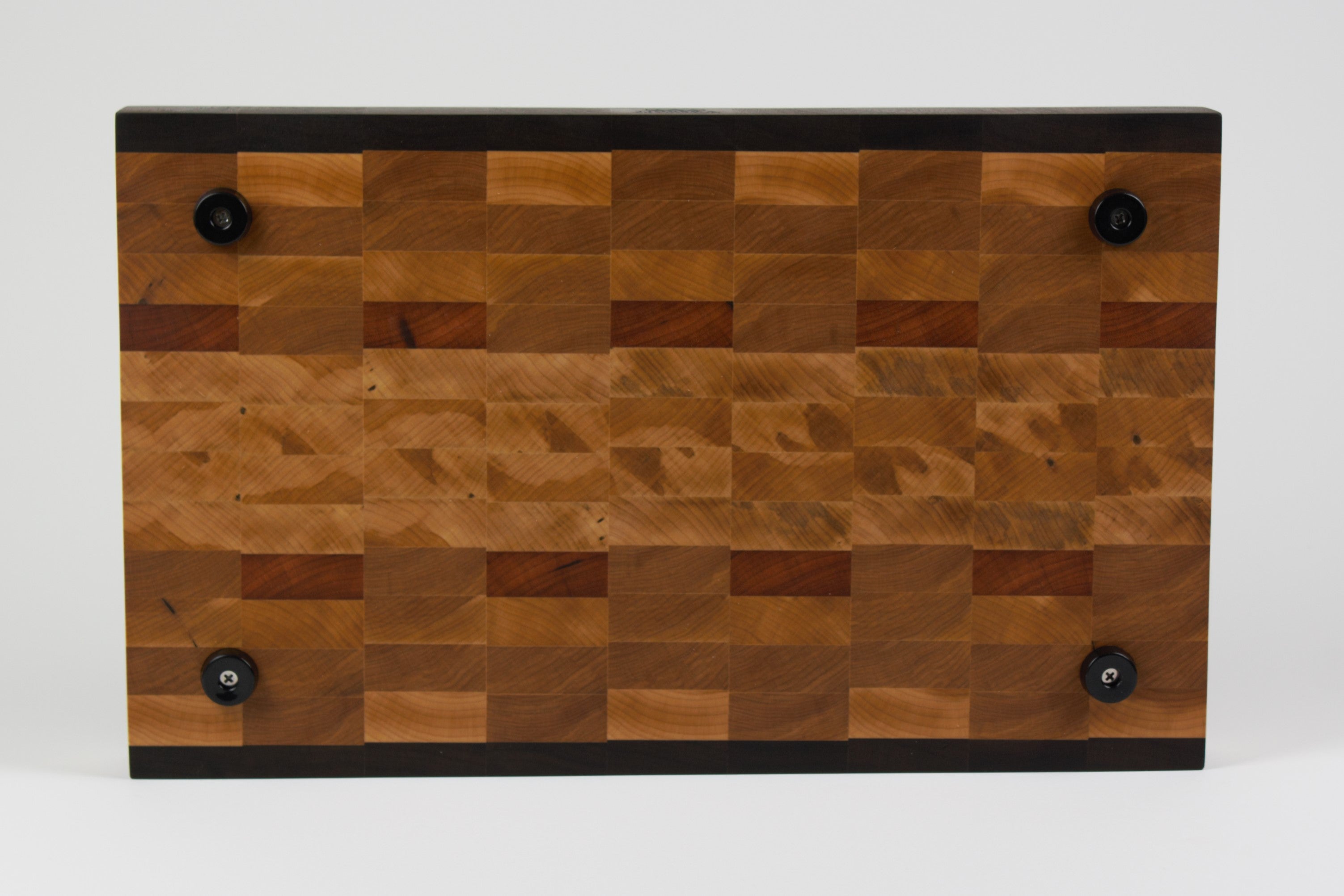 End grain cutting board made of rustic Hard Maple and accented with Tigerwood and Black Walnut. Straight on view of the bottom surface. Four cutting board feet mounted to board surface.