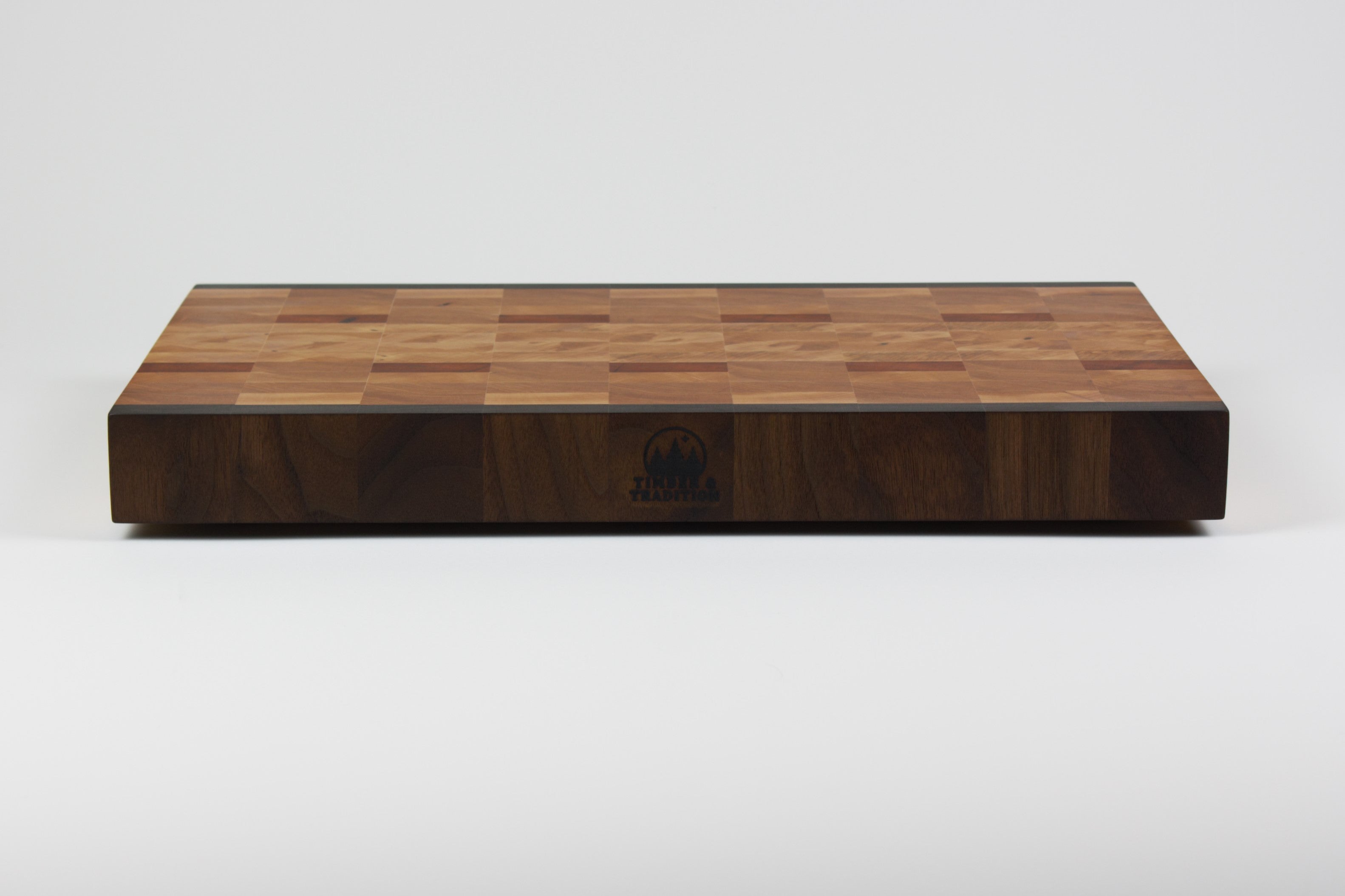 End grain cutting board made of rustic Hard Maple and accented with Tigerwood and Black Walnut. Front center view with the Timber & Tradition logo burned into front of board.