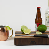 Timber & Tradition branded cutting board with cut limes, ginger beer, and Mezcal to prepare a Mezcal mule.