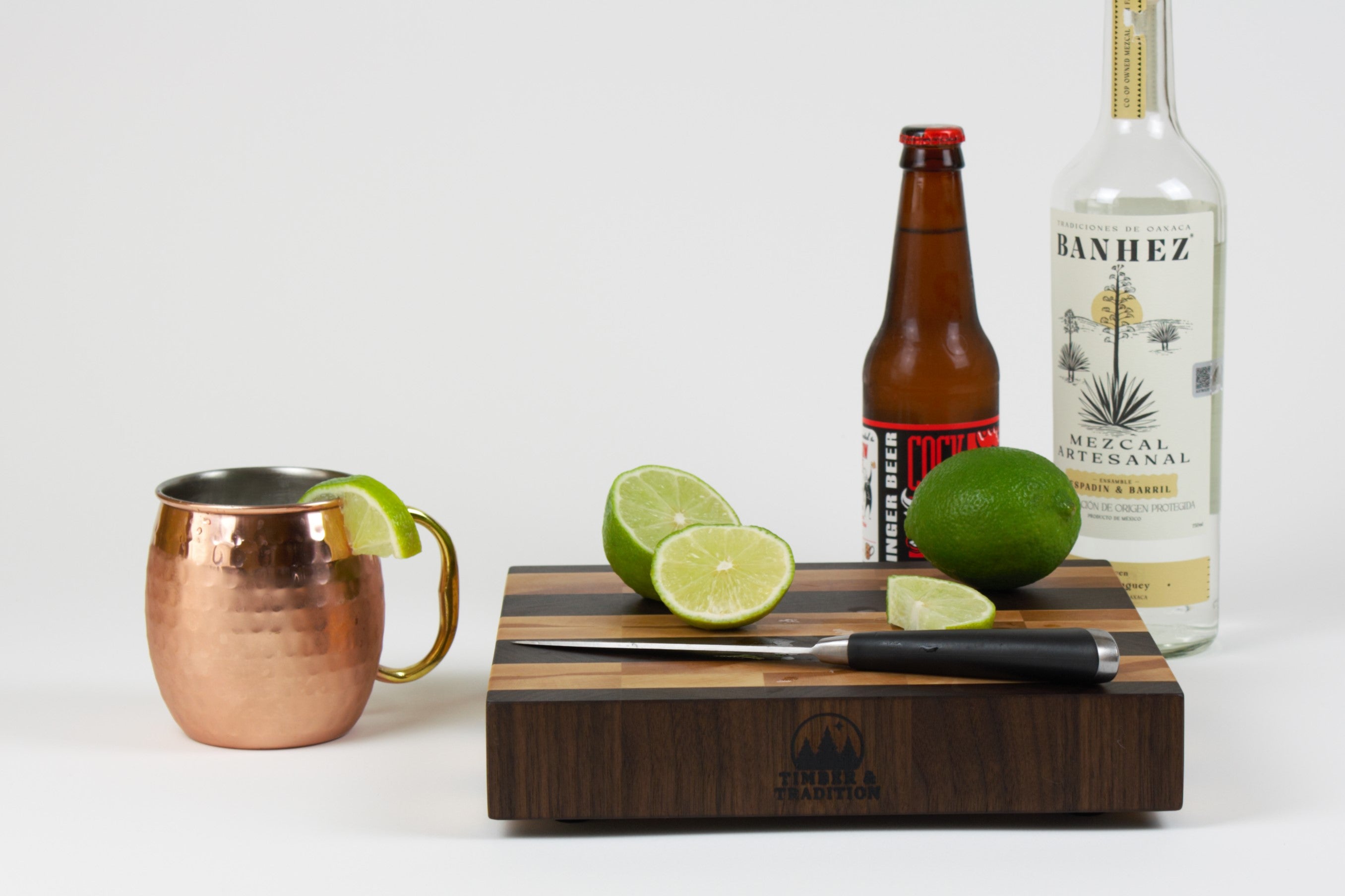 Timber & Tradition branded cutting board with cut limes, ginger beer, and Mezcal to prepare a Mezcal mule.