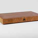 Cherry wood end grain cutting board with rich warm wood tones.  Timber & Tradition logo burned into center front. Front left corner view.
