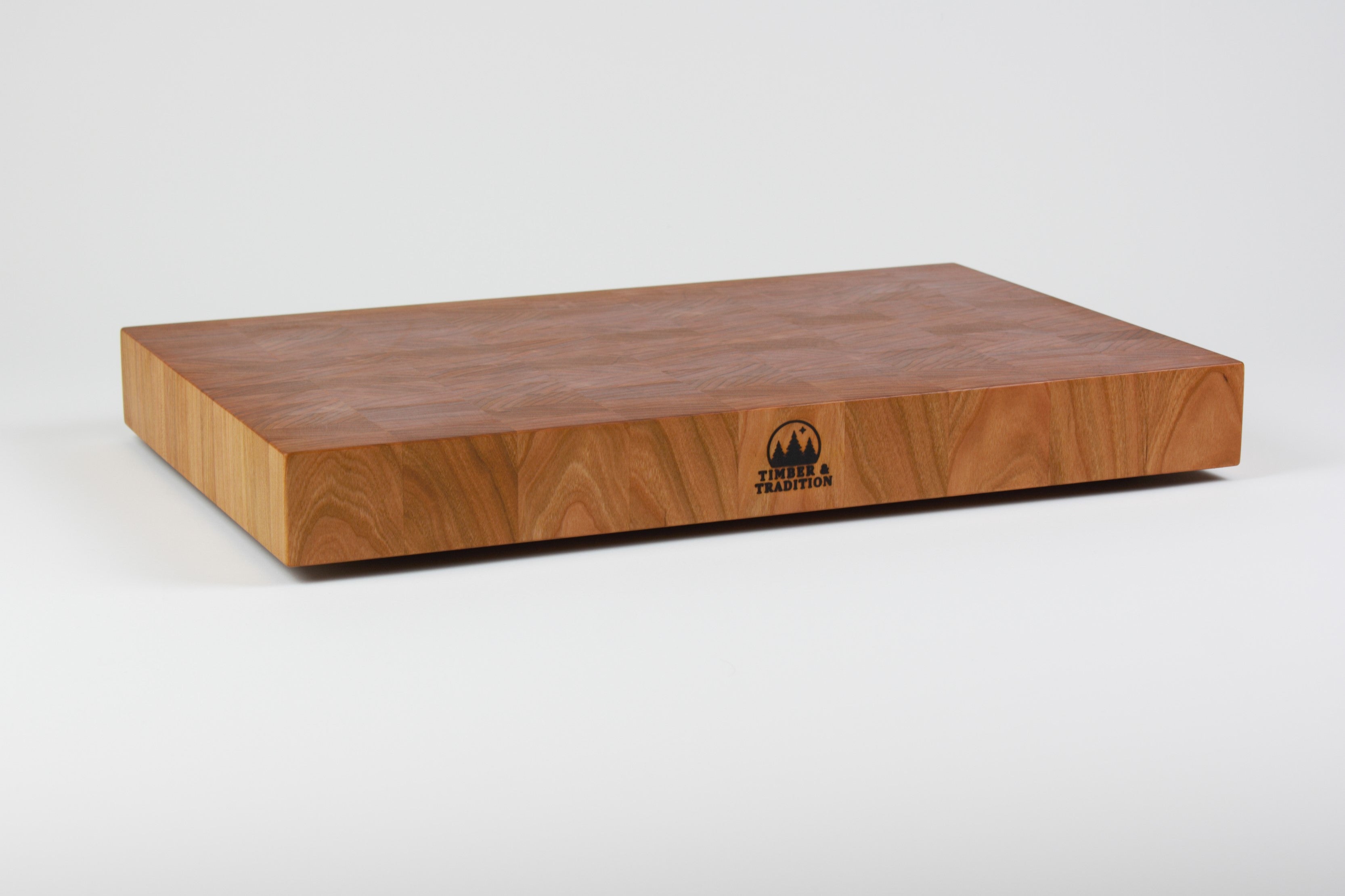 Cherry wood end grain cutting board with rich warm wood tones.  Timber & Tradition logo burned into center front. Front left corner view.