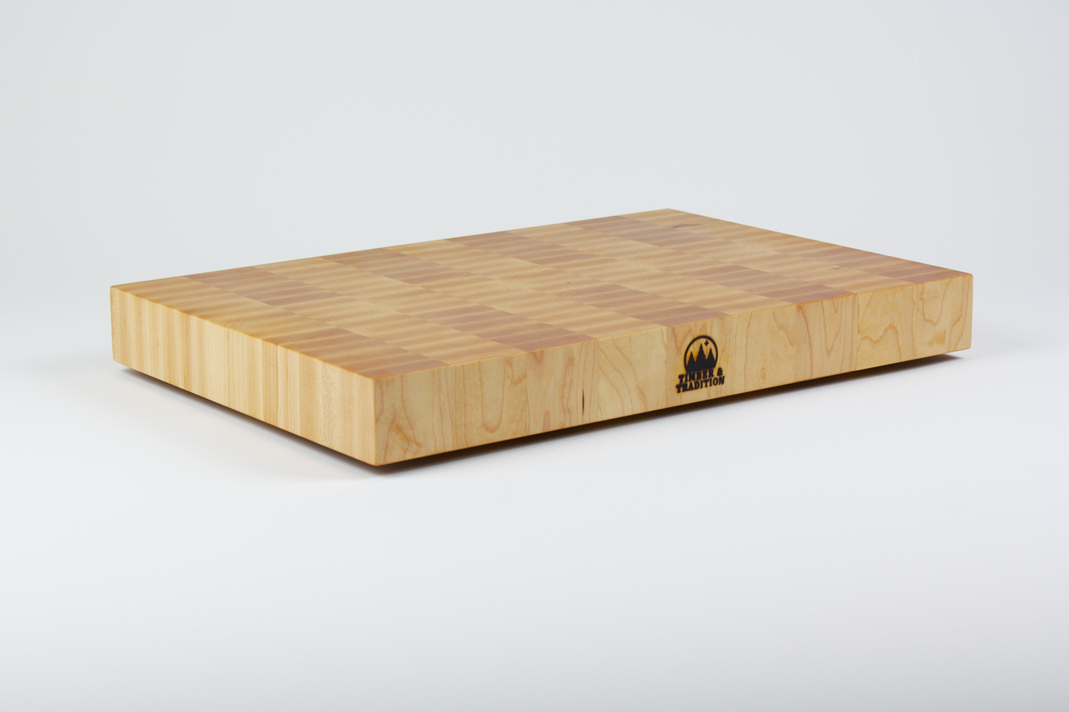 Classic Hard Maple cutting board with golden hues. The Timber & Tradition logo is burned into the center front, this is the front left corner view.