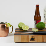 Maple and Black Walnut cutting board with cut limes, ginger beer, and Mezcal to prepare a Mezcal mule.