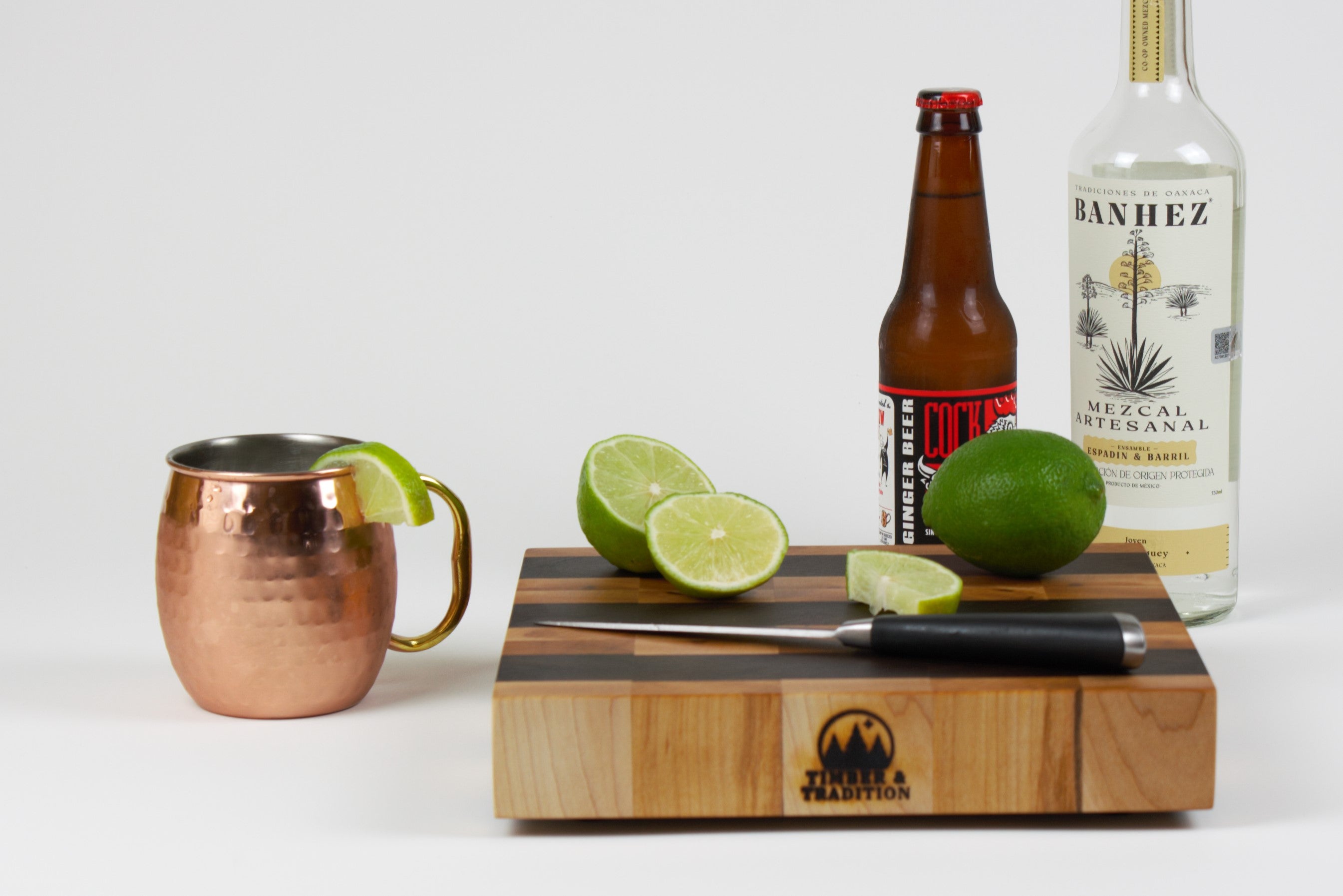 Maple and Black Walnut cutting board with cut limes, ginger beer, and Mezcal to prepare a Mezcal mule.