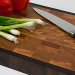 End grain cutting board made of rustic Hard Maple and accented with Tigerwood and Black Walnut. Red peppers and scallions lay on the cutting surface next to a chef's knife.