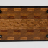 End grain cutting board made of rustic Hard Maple and accented with Tigerwood and Black Walnut. Straight on view of the bottom surface. Four cutting board feet mounted to board surface.